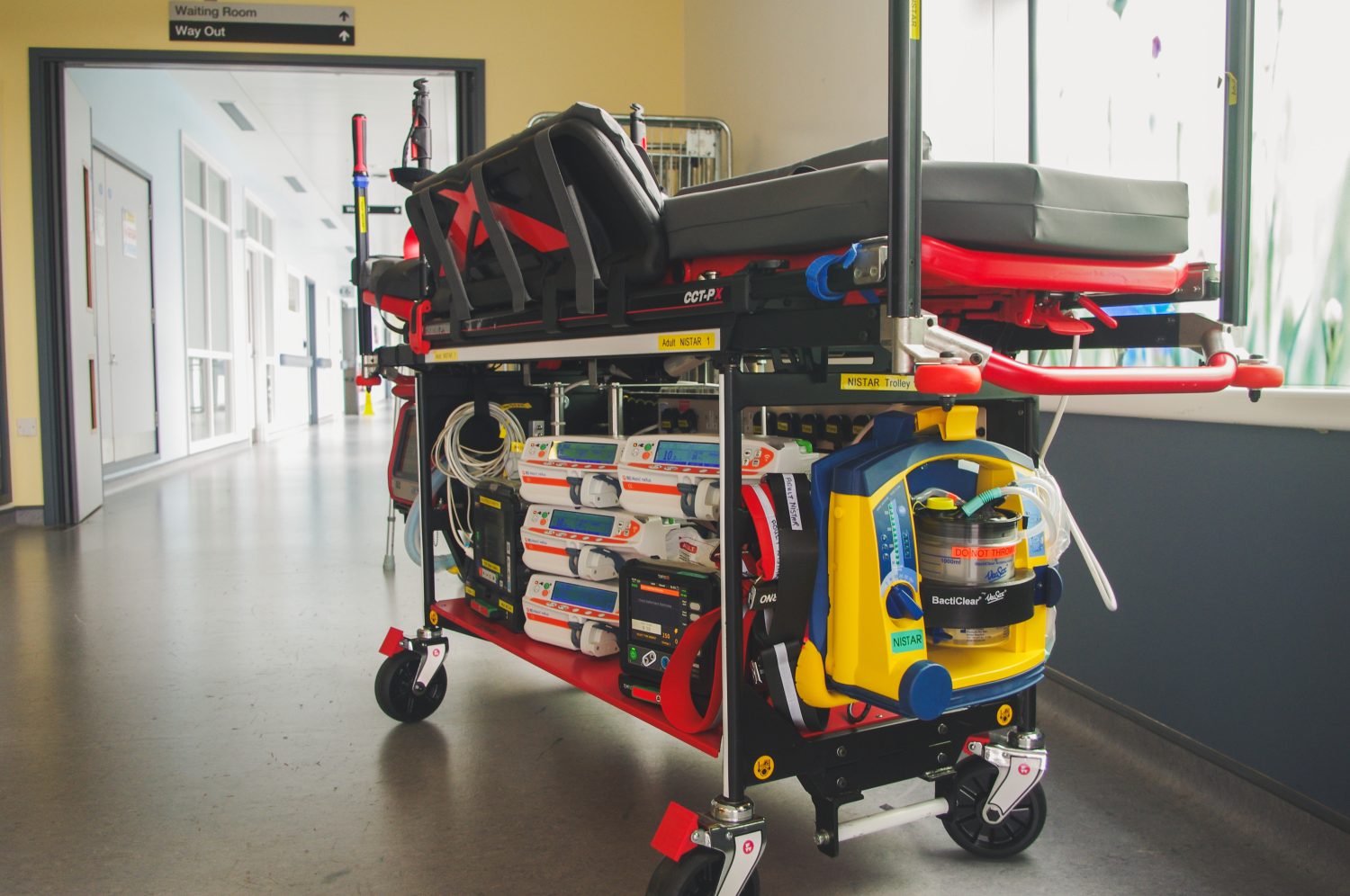 Close up photo of adult transport trolley with suction machine at the end, and syringe drivers and defibrillator under trolley.